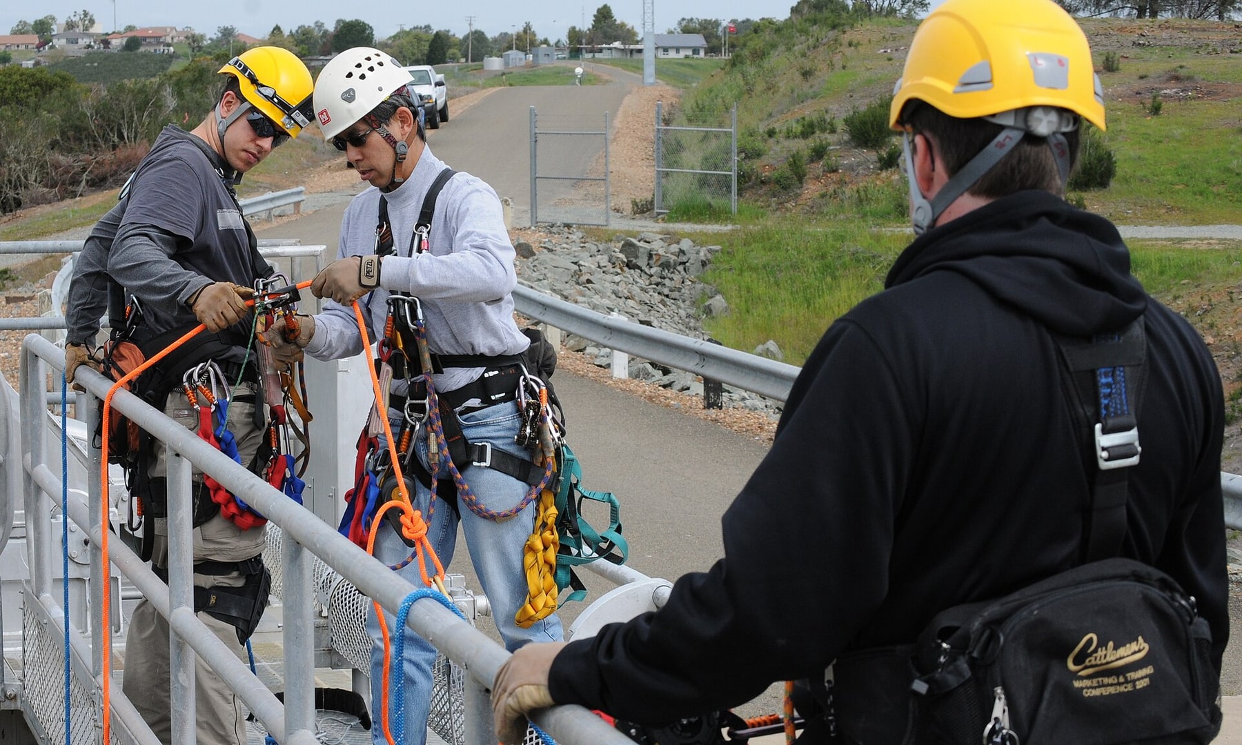Three engineers prepare climbing equipment before a dam-gate inspection.
