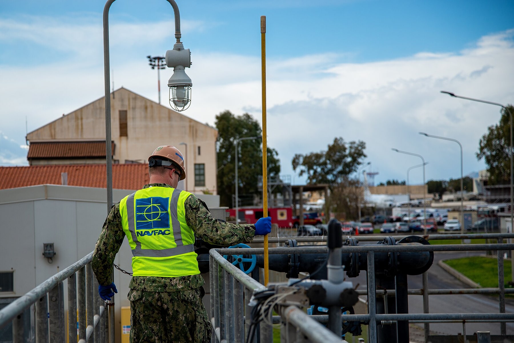 A wastewater-treatment worker uses a long-handled tool beside the facility's pipes.