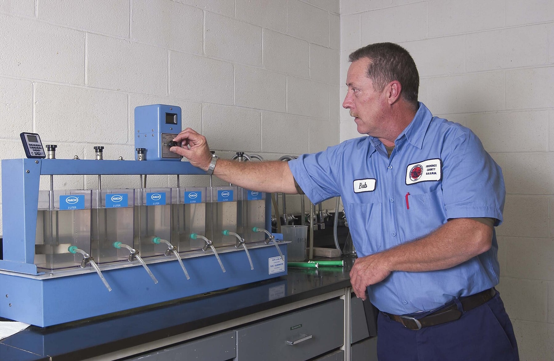 A drinking-water operator adjusts jar-testing equipment used to compare treatment conditions.